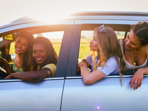 Happy friends of four women smiling inside rental car during Kenya road trip adventure at sunset